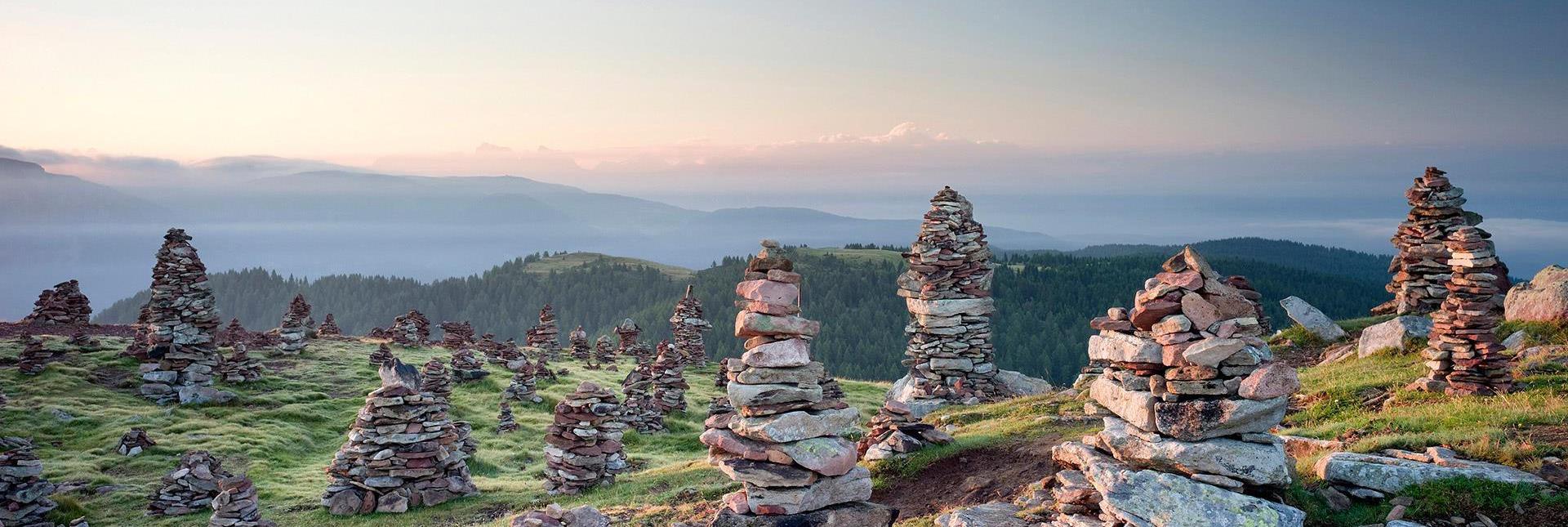 Ommini di pietra su un prato alpino all’alba con vista su colline e montagne sullo sfondo