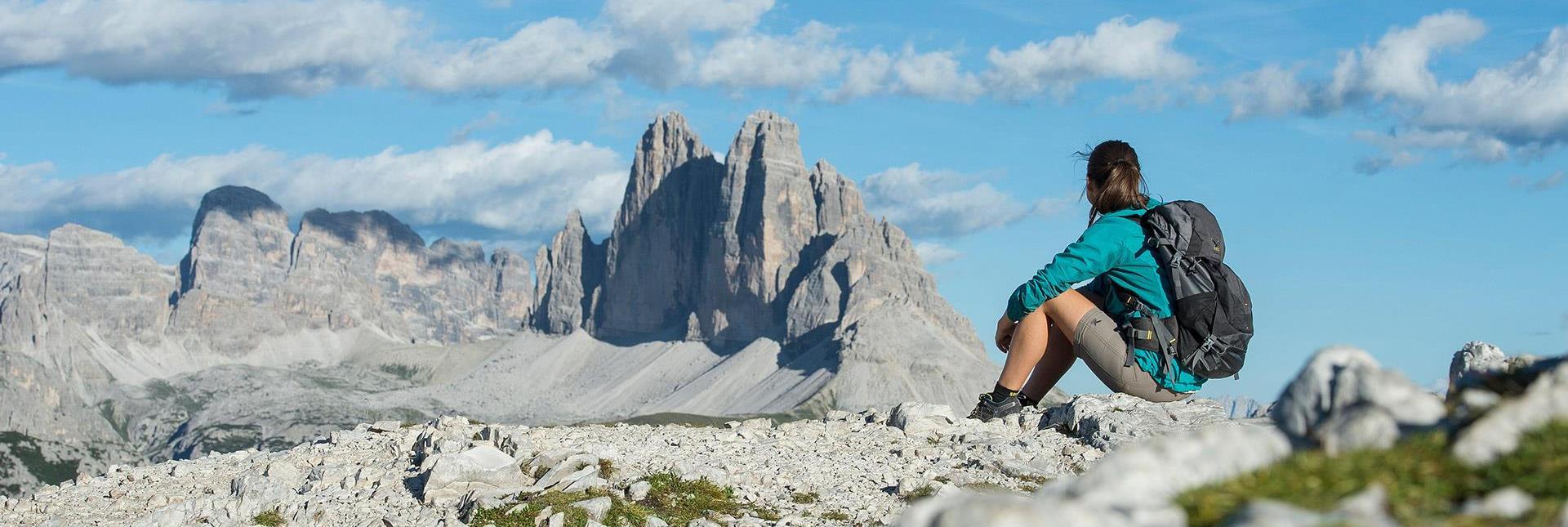 Un'escursionista è seduta su una roccia e guarda le Tre Cime